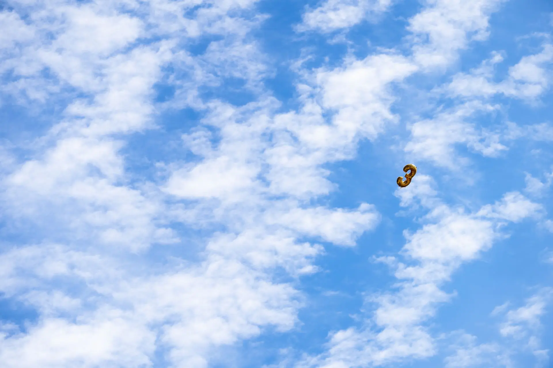 Flying Three A birthday balloon against blue sky and clouds